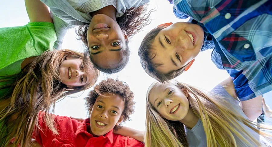 The faces of five pre-teens standing in a circle looking down at the camera.