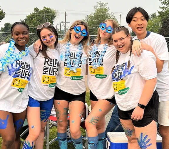 A group of friends stand next to each other. They are wearing Relay for Life shirts and smiling.