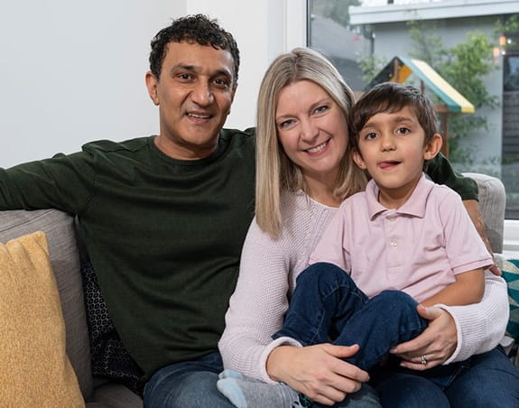 A mother, father and their young son cuddle together on a couch