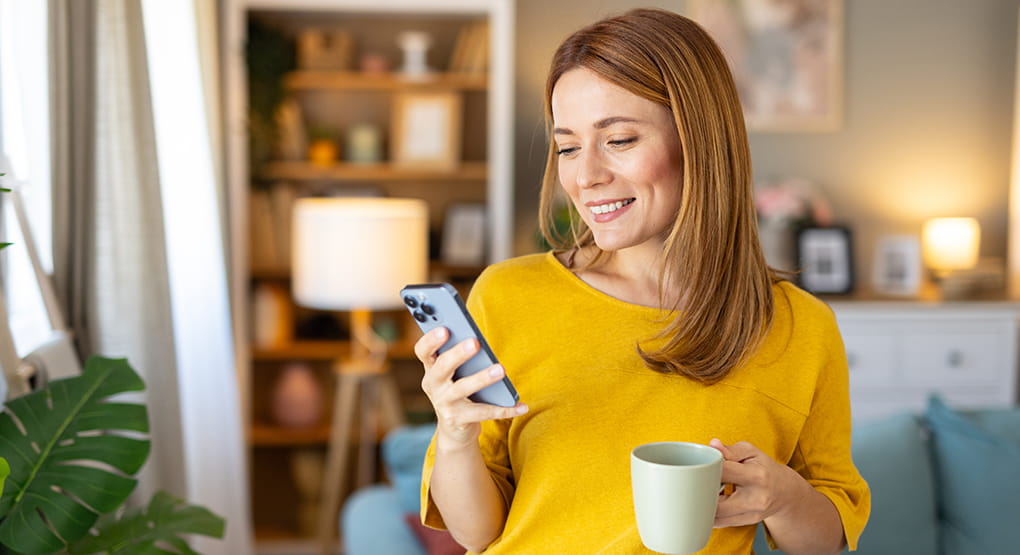 A person in their home looks at their  phone and smiles.  