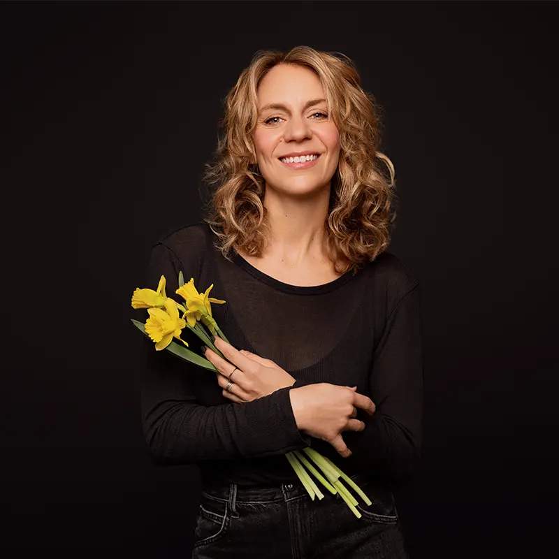 Léane Labrèche-Dor standing, holding a bouquet of yellow daffodils, wearing a black top, against a dark background