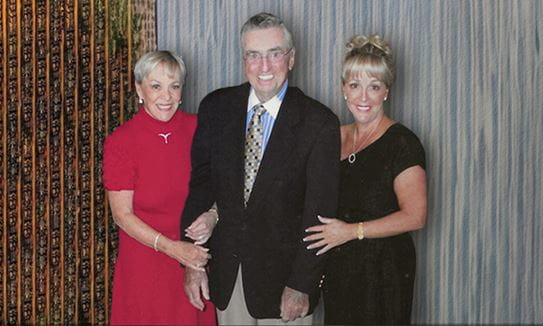 Three people in formal clothing standing together smiling.