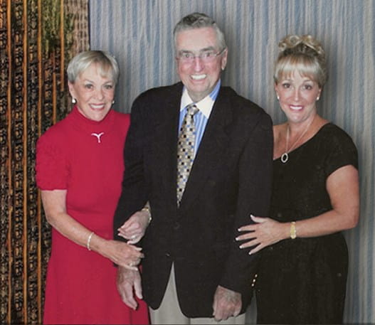 Three people in formal clothing standing together smiling.