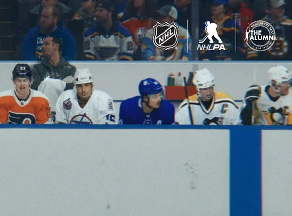A hockey game with players sitting on the bench and the NHL, NHLPA and The Alumni logos.