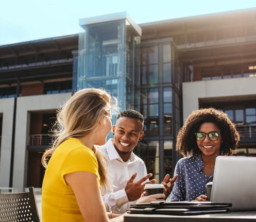 Four people sit outside working at a table, they are smiling as they talk with each other