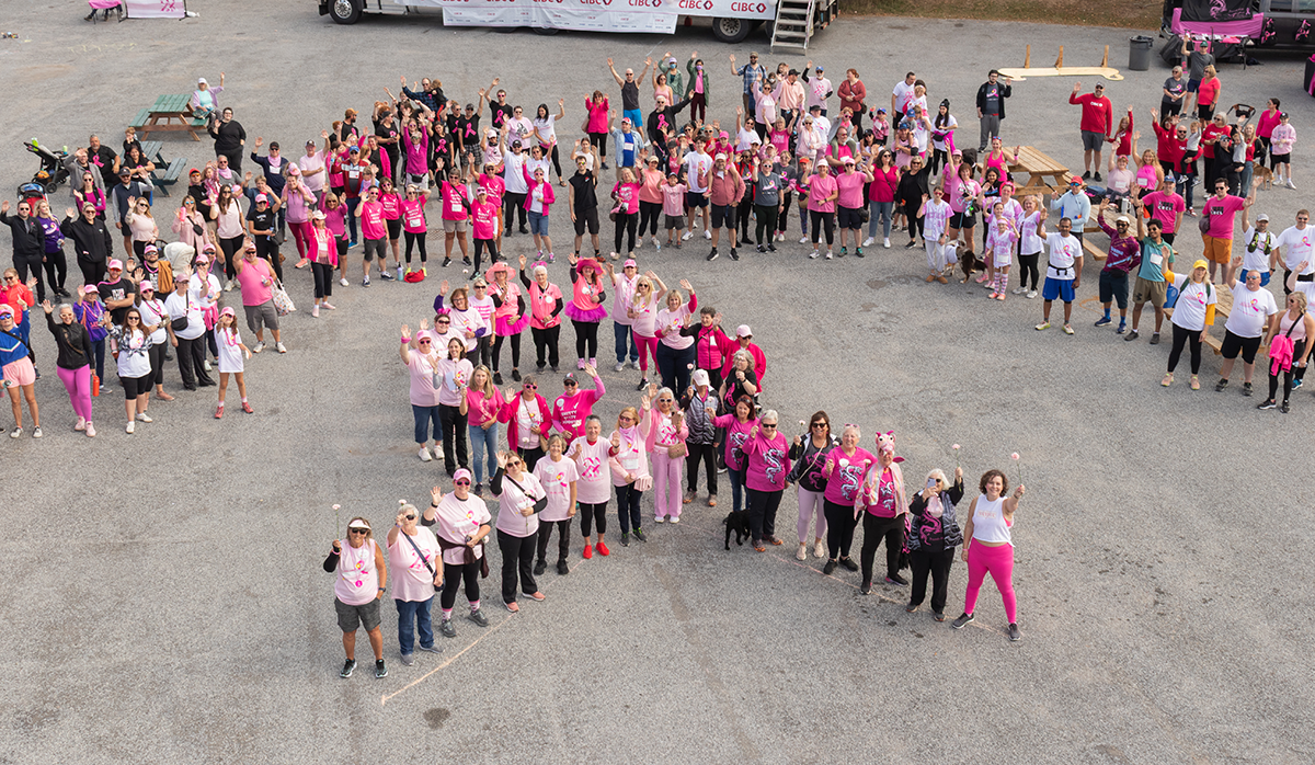 Group of people wearing pink shirts forming a ribbon shape outdoors.