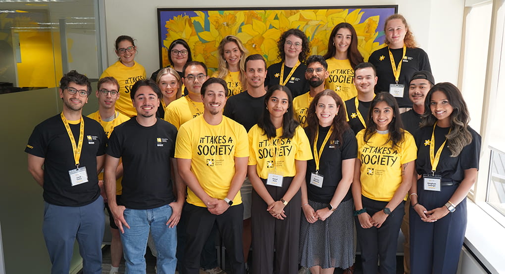 Group of people wearing matching yellow and black shirts with the text ‘It Takes a Society.’
