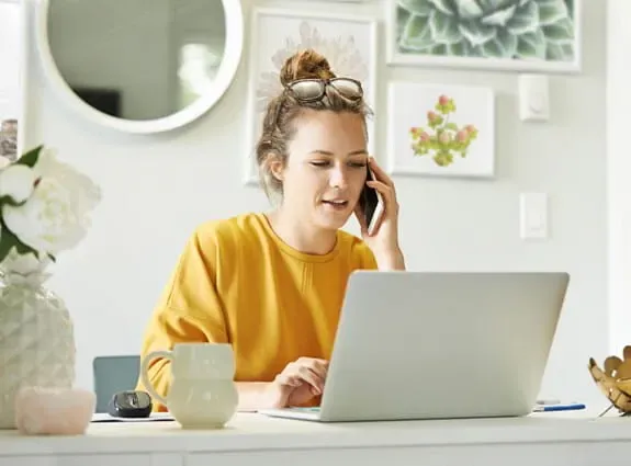 A young woman on her laptop computer and on her cell phone at home