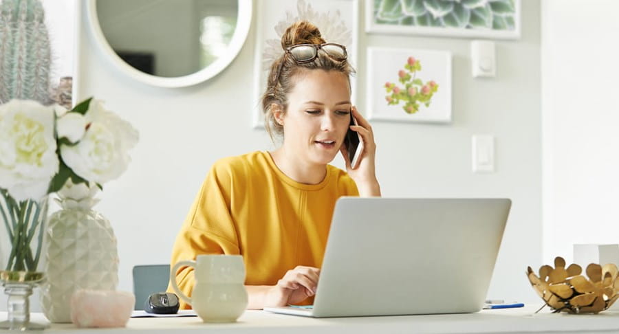 Une jeune femme sur son ordinateur portable et sur son téléphone portable à la maison