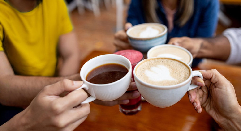 Quatre personnes trinquant avec leurs tasses à café