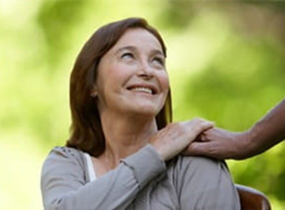 A woman looks back and up at a person who has placed their hand on her shoulder