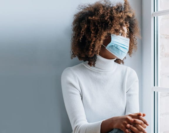 Women wearing a mask looking out a window