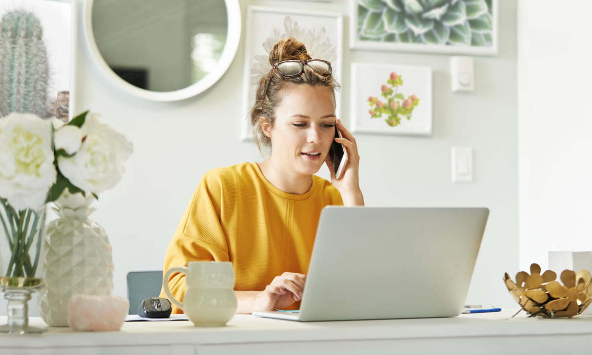 Une jeune femme utilisant son ordinateur portable et son téléphone portable chez elle.