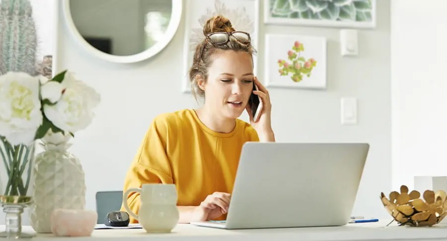 Une jeune femme utilisant son ordinateur portable et son téléphone portable chez elle.
