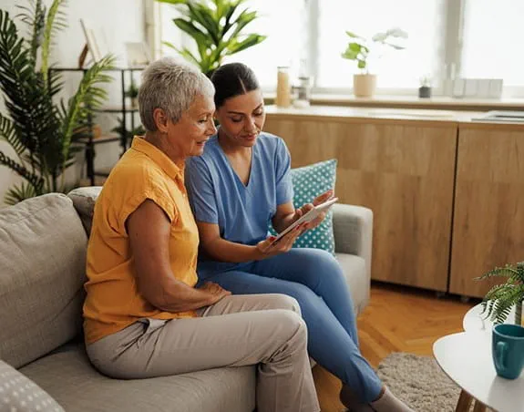 Two people sit on a couch in a living room looking at a tablet together.