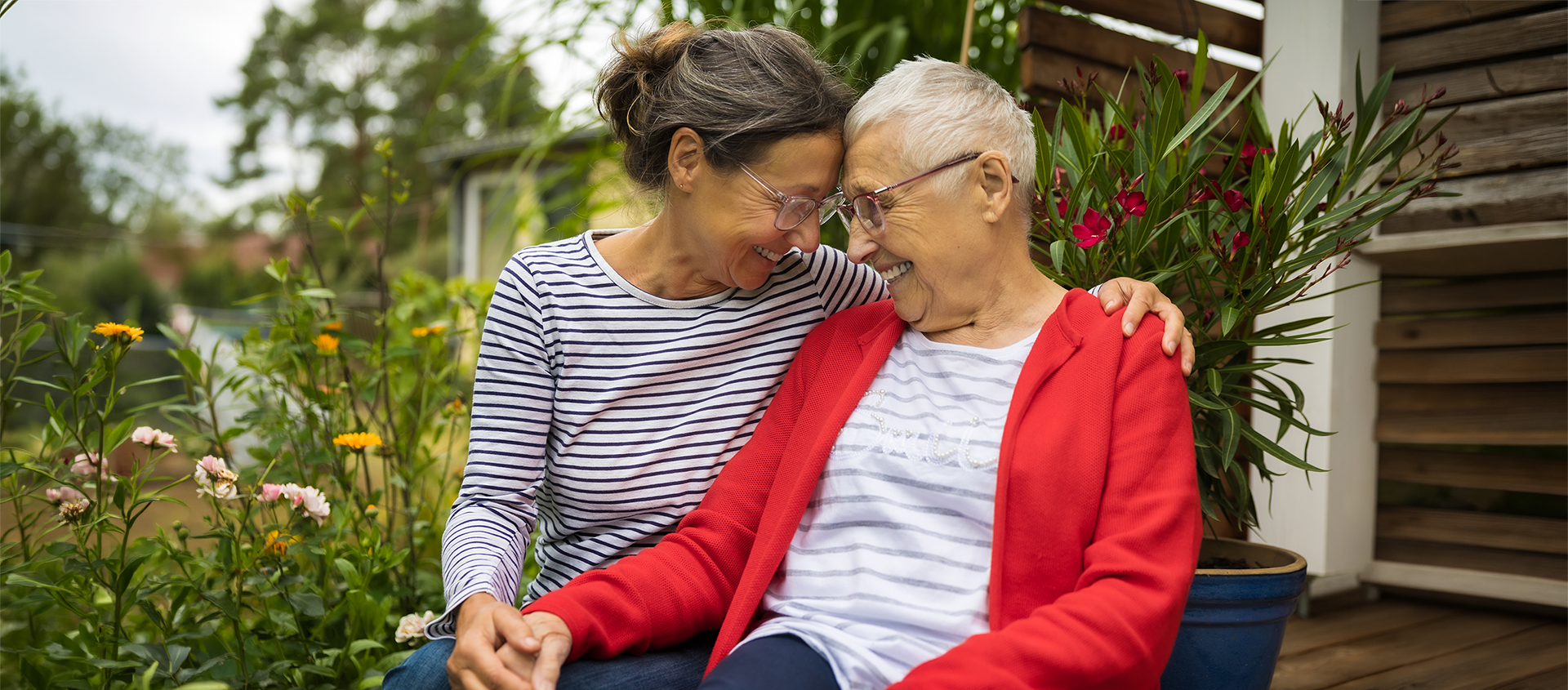 An older adult is embraced by a younger family member. They are sitting outside together.