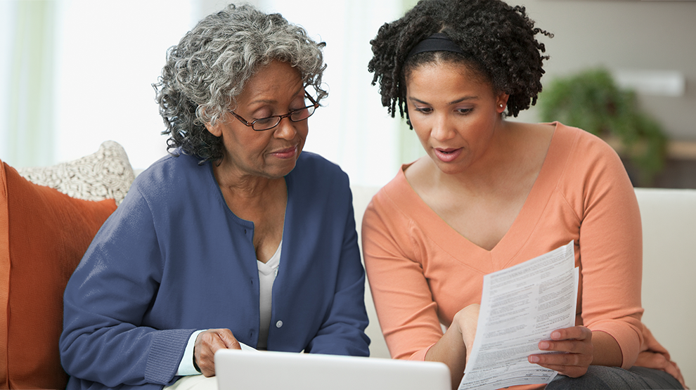 Une personne adulte âgée regarde des papiers avec une membre plus jeune de la famille.