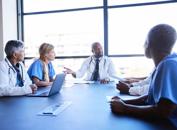 Un groupe de professionnels de la santé sont assis autour d’une table de conférence dans une pièce lumineuse et discutent.
