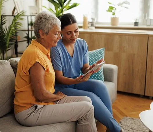 Two people sit on a couch in a living room looking at a tablet together.
