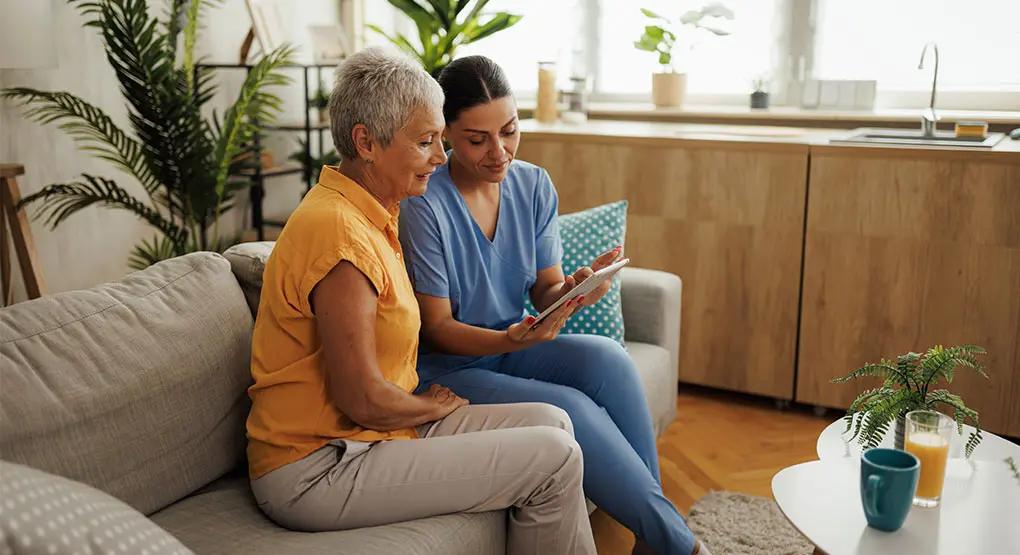 Two people sit on a couch in a living room looking at a tablet together.