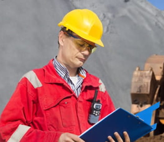 Outdoor worker checks paperwork on clipboard at construction site