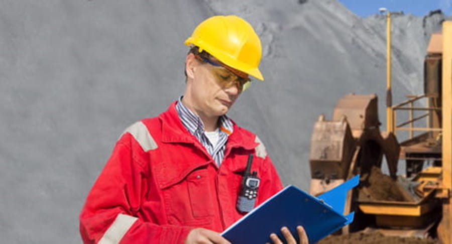 Outdoor worker checks paperwork on clipboard at construction site