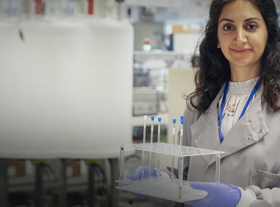 Une chercheuse portant une blouse de laboratoire et tenant des flacons sur un plateau.