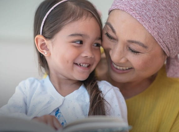 A young girl is reading a book to an older woman wearing a headscarf