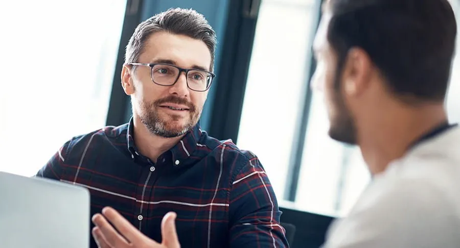 Two men talking in front of a laptop