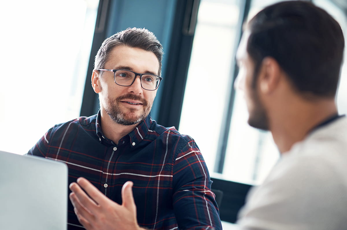Deux hommes discutent devant un ordinateur portable.