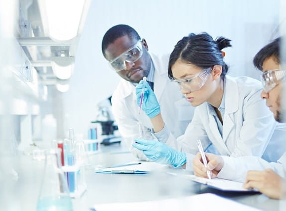 A female researcher in a lab, working with 2 other male researchers.