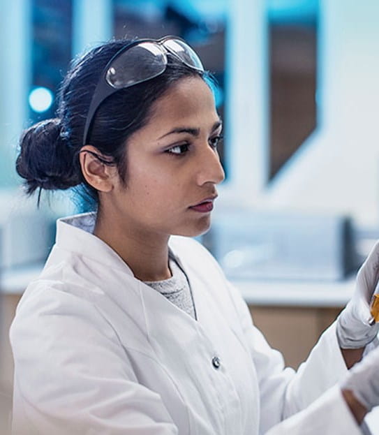 A female cancer researcher typing into a touch screen and holding a vial in a lab.