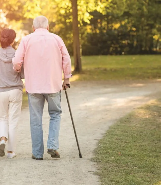 A woman and an elderly man walking with a cane.
