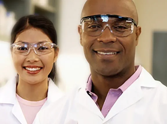Two cancer researchers wearing lab coats and safety glasses
