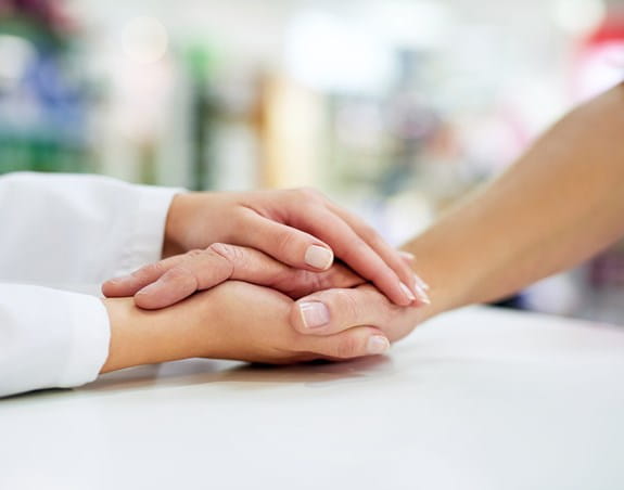 An older persons hand is being embraced by the hands of a younger person