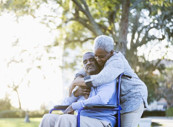 A woman is hugging a man who is sitting in a wheelchair