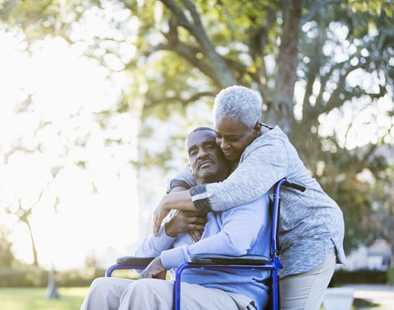 A woman is hugging a man who is sitting in a wheelchair