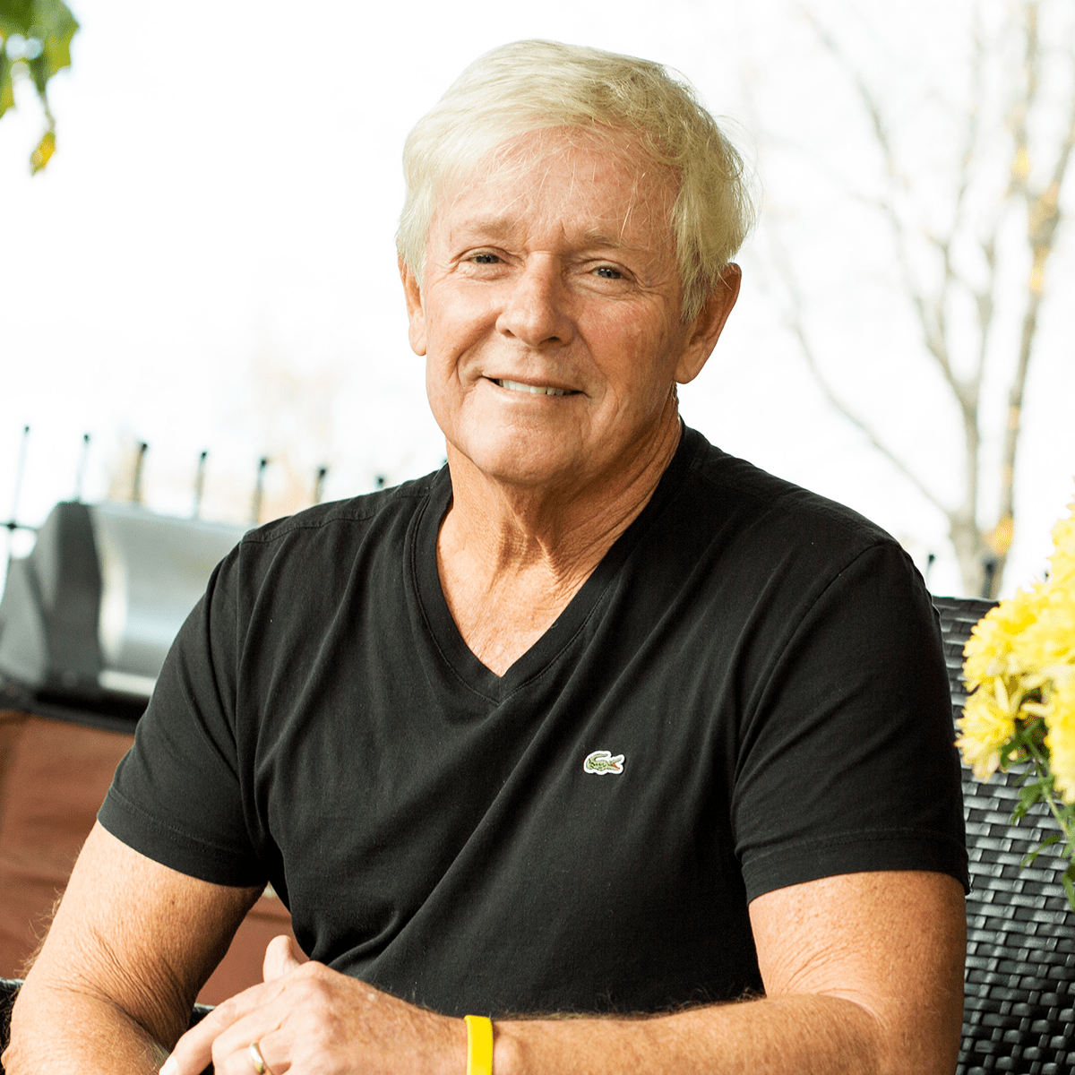 Headshot of Jack Shore, a man with tan skin and white hair wearing a black T-shirt and a yellow rubber band bracelet