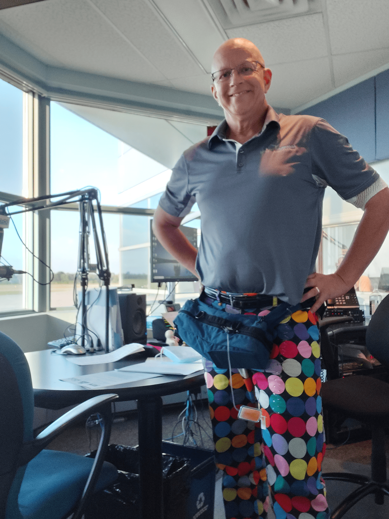Terry Johnston est debout dans un bureau. Il porte un polo bleu clair et un pantalon à pois multicolores. 