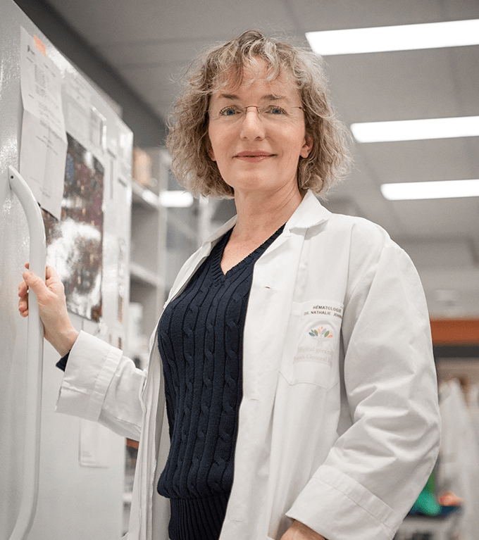 La Dre Nathalie Johnson, une femme à la peau claire, aux cheveux blonds et vêtue d’un sarrau, est debout et tient la poignée du réfrigérateur du laboratoire  