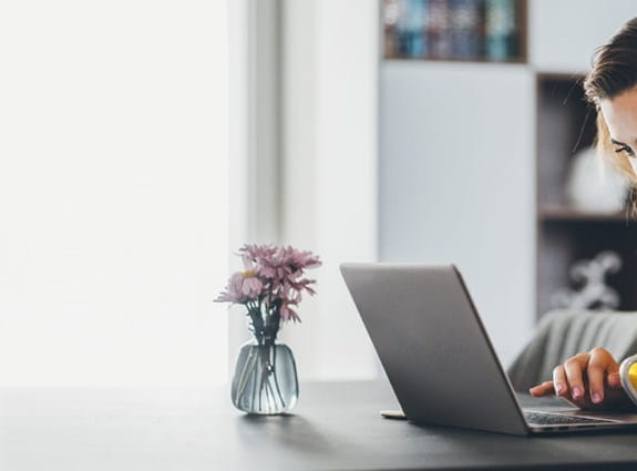 a woman sits at her kitchen table working on her laptop