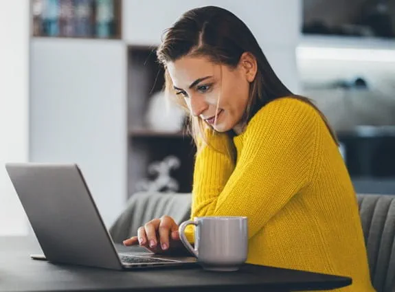 a woman sits at her kitchen table working on her laptop