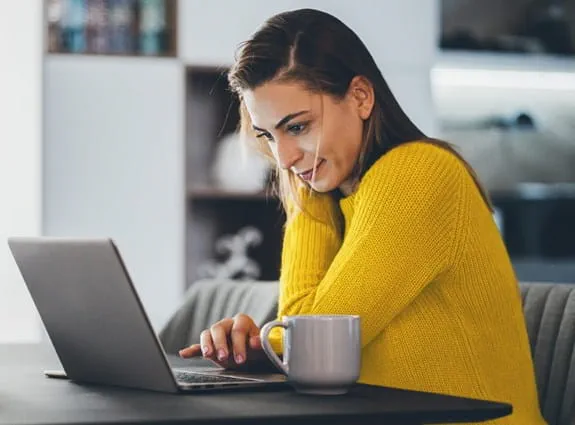 Femme assise à une table de cuisine, travaillant sur un ordinateur portable.