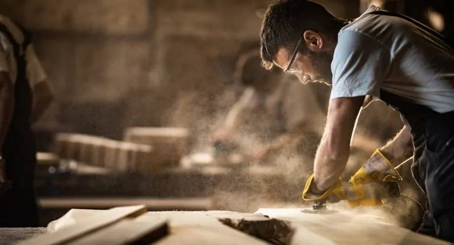 A man is on a worksite sanding a wooden board with power tools