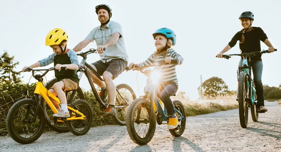 A father mother and their two children are riding their bikes down a path