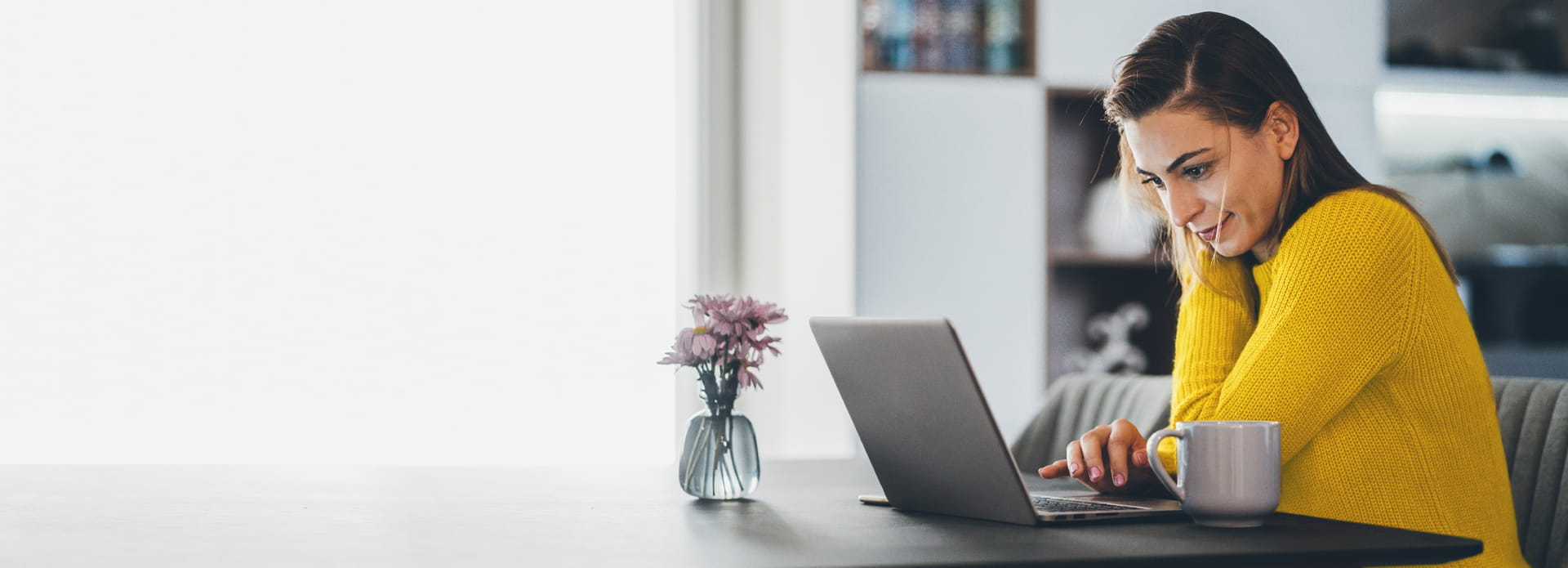 Femme assise à une table de cuisine, travaillant sur un ordinateur portable.