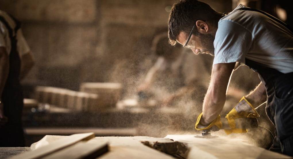 Homme sur un chantier en train de poncer une pièce de bois à l’aide d’un outil électrique.