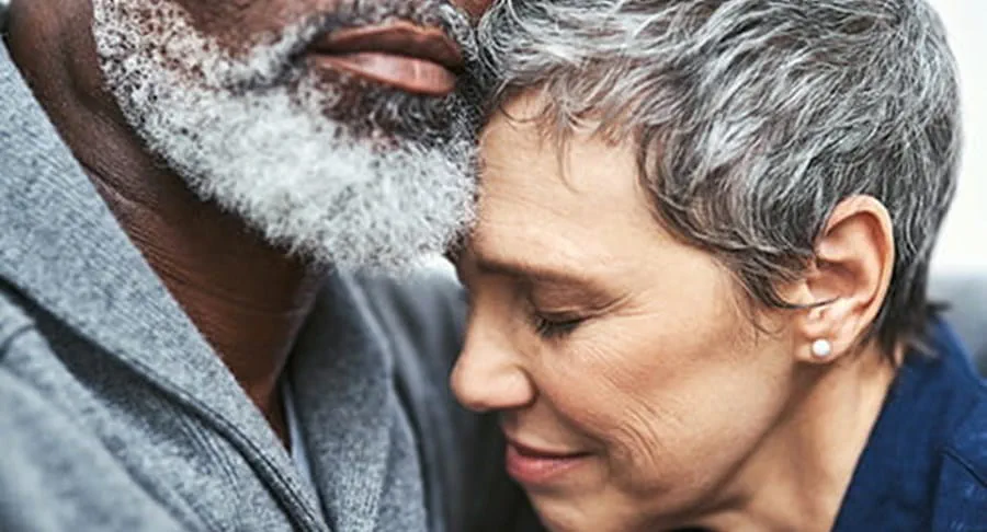 The face of a woman with short grey hair looking sad, hugging a man with a beard