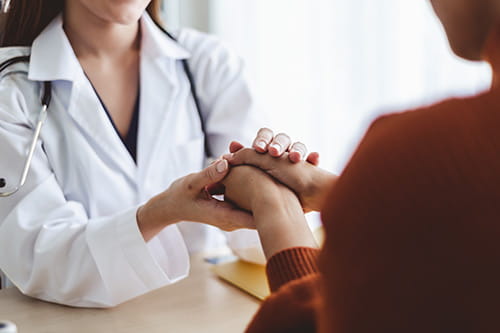 A doctor is embracing their patients hands while they are speaking with them