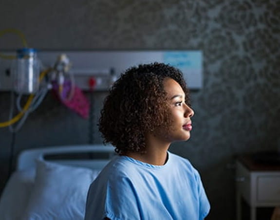 A woman sits on a hospital bed in a hospital gown